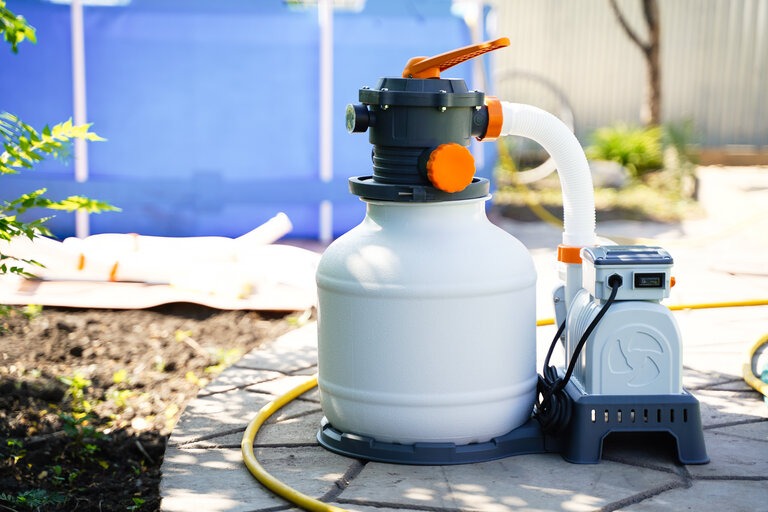 Sandfilteranlage zur Reinigung von Schwimmbadwasser vor dem Hintergrund eines Polyethylen-Rahmenbeckens.