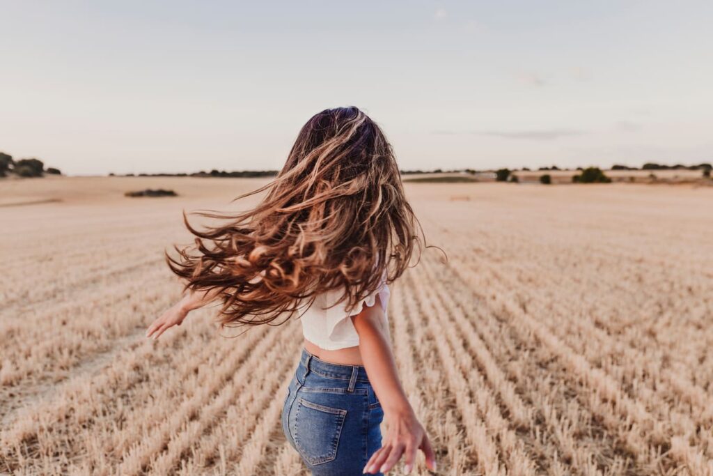 Eine Frau mit langen, lockigen Haaren, die durch ein Feld läuft, zeigt die Freiheit und den natürlichen Look, den Haarteile bieten können.