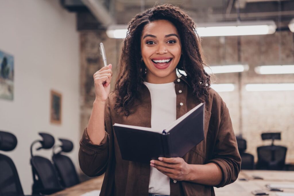 Junge Frau mit Notizbuch und Stift in einem kreativen Büro, symbolisch für Ideenfindung und innovative Ansätze bei Lampenfassungen