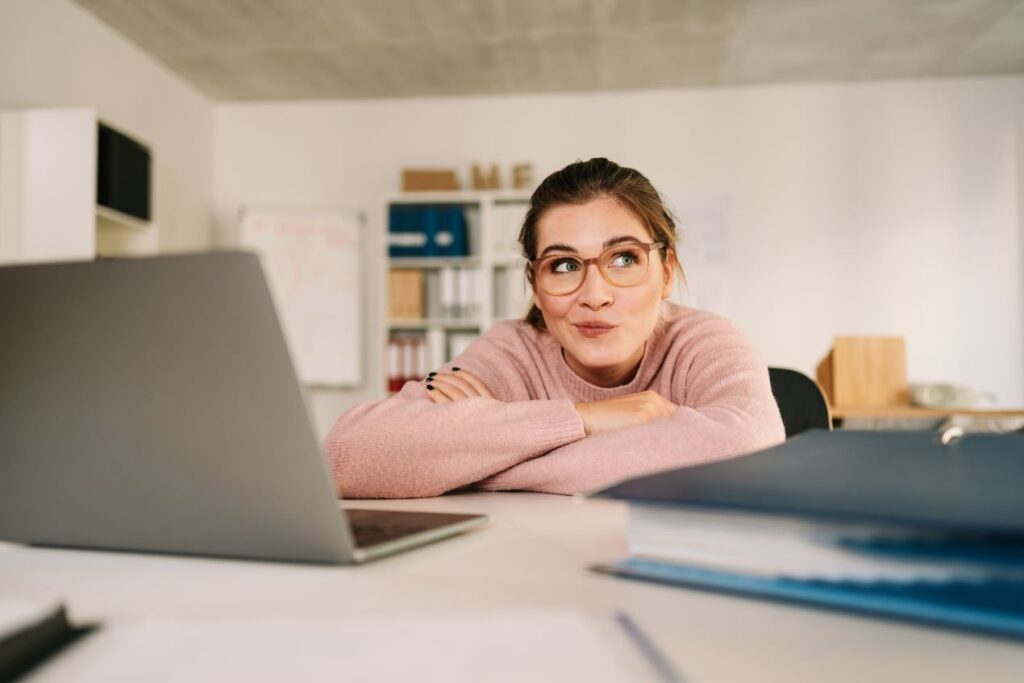 Junge Frau in einem modernen Büro, die nachdenklich lächelt, symbolisch für kreative Gedanken und Designideen zu Lampenfassungen