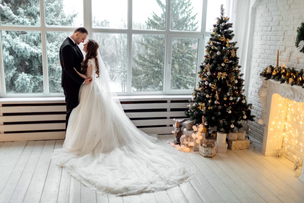 Junges verliebtes Brautpaar posiert im Studio auf dem mit Weihnachtsbaum geschmückten Hintergrund an ihrem Hochzeitstag