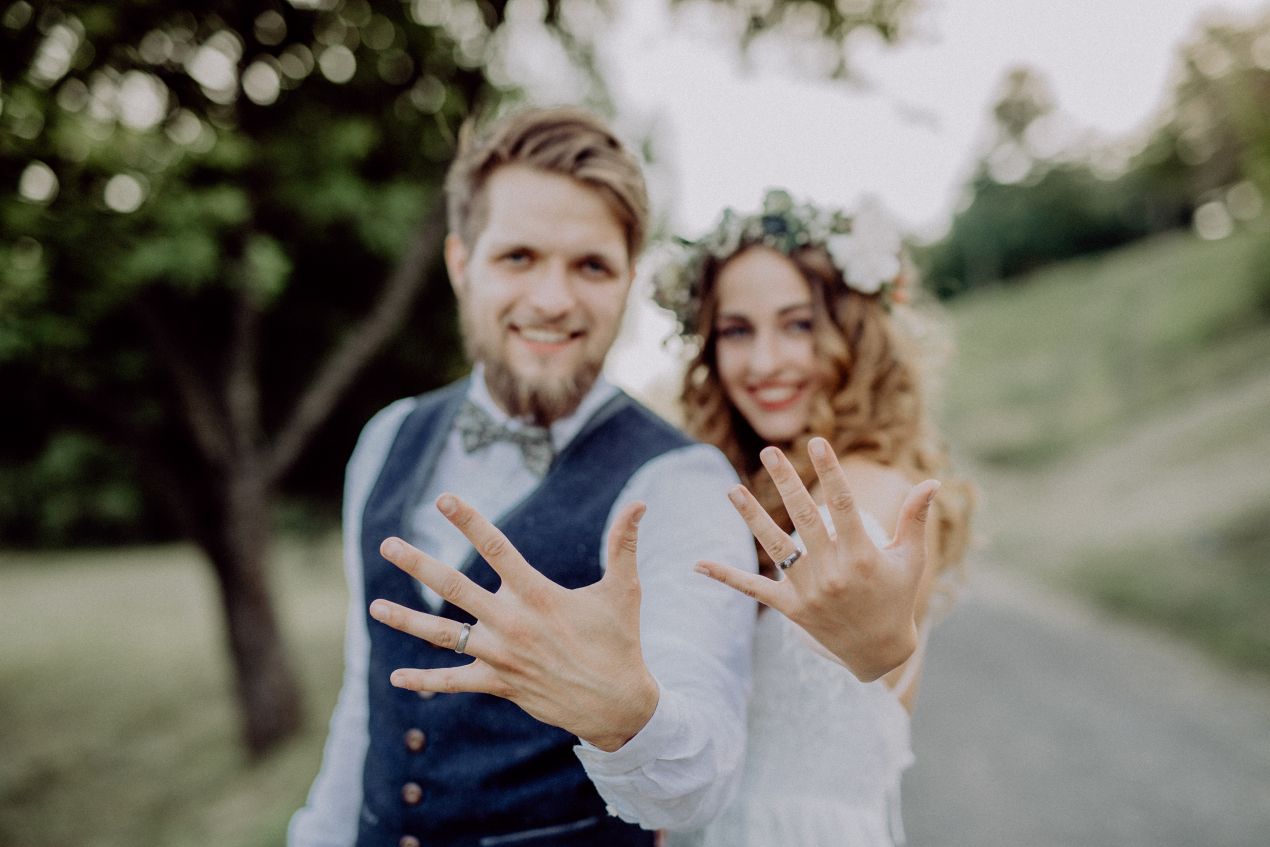 Brautpaar zeigt stolz Eheringe bei moderner Hochzeit im Gruenen – Trauring Konfigurator zur Auswahl nutzen