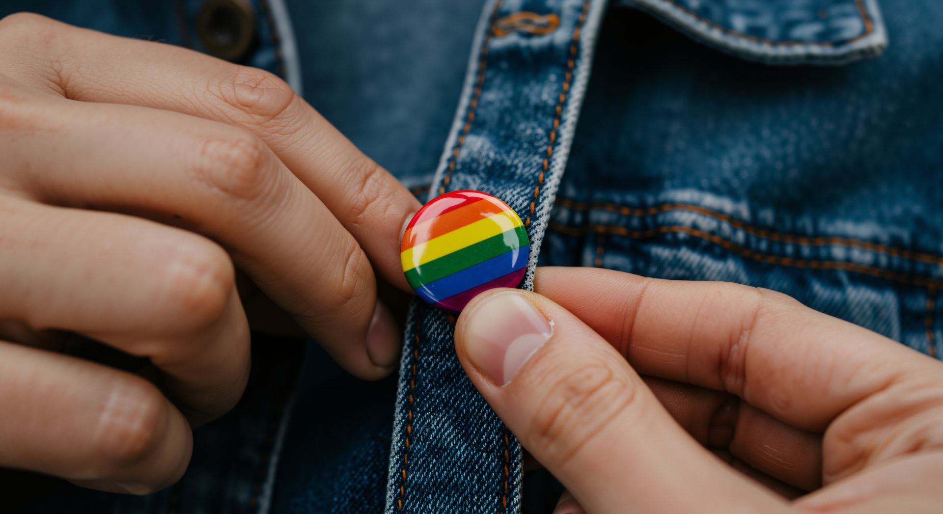 Hand befestigt einen bunten Button mit Regenbogenmotiv an einer Jeansjacke als Ausdruck von Individualität