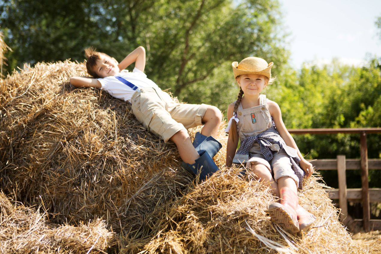 Kinder sitzen und liegen auf Strohballen, lachend und entspannt bei einem Ausflug zu einem Erlebnisbauernhof NRW